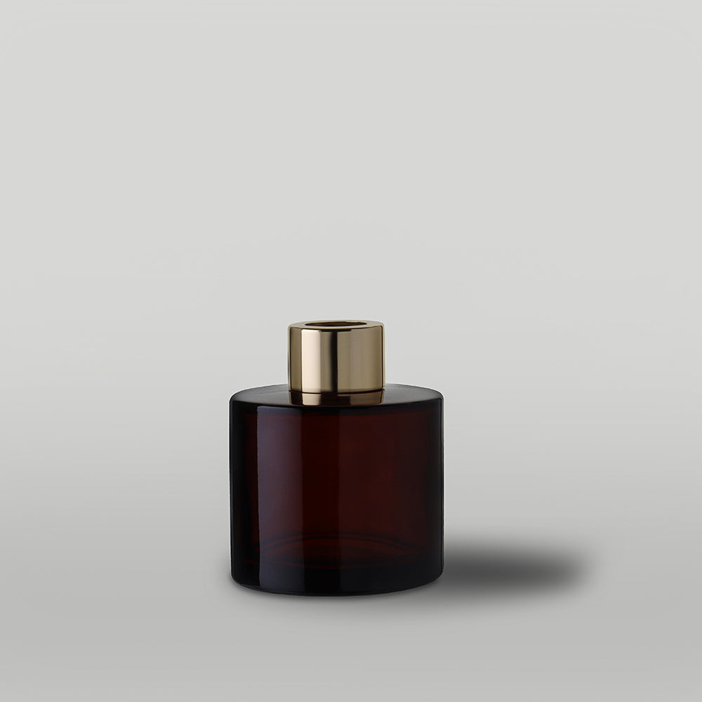 Amber glass diffuser bottle with gold cap on a light gray background