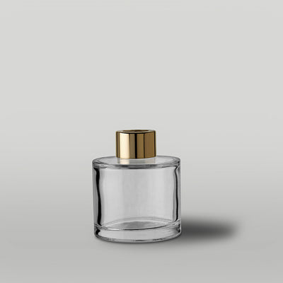 Clear glass diffuser bottle with a gold top on a light gray background
