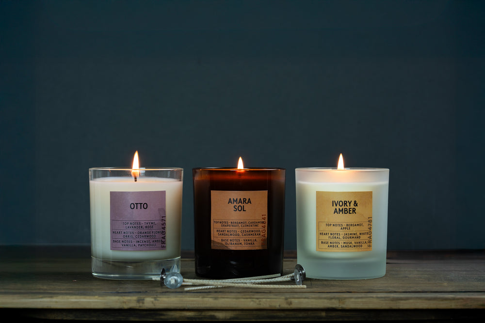 Three lit candles with labels on a wooden surface against a dark background