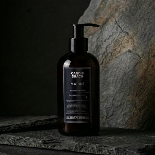 Black bottle hand and body wash 'Candle Shack Marine' on a dark stone surface with a stone wall background