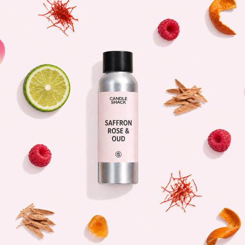 A silver aluminum spray bottle labeled 'Candle Snacks Saffron Rose & Oud' is centered on a pale pink background, surrounded by decorative botanical and citrus props including star anise, raspberries, lime slices, orange peels, and pink rose petals.