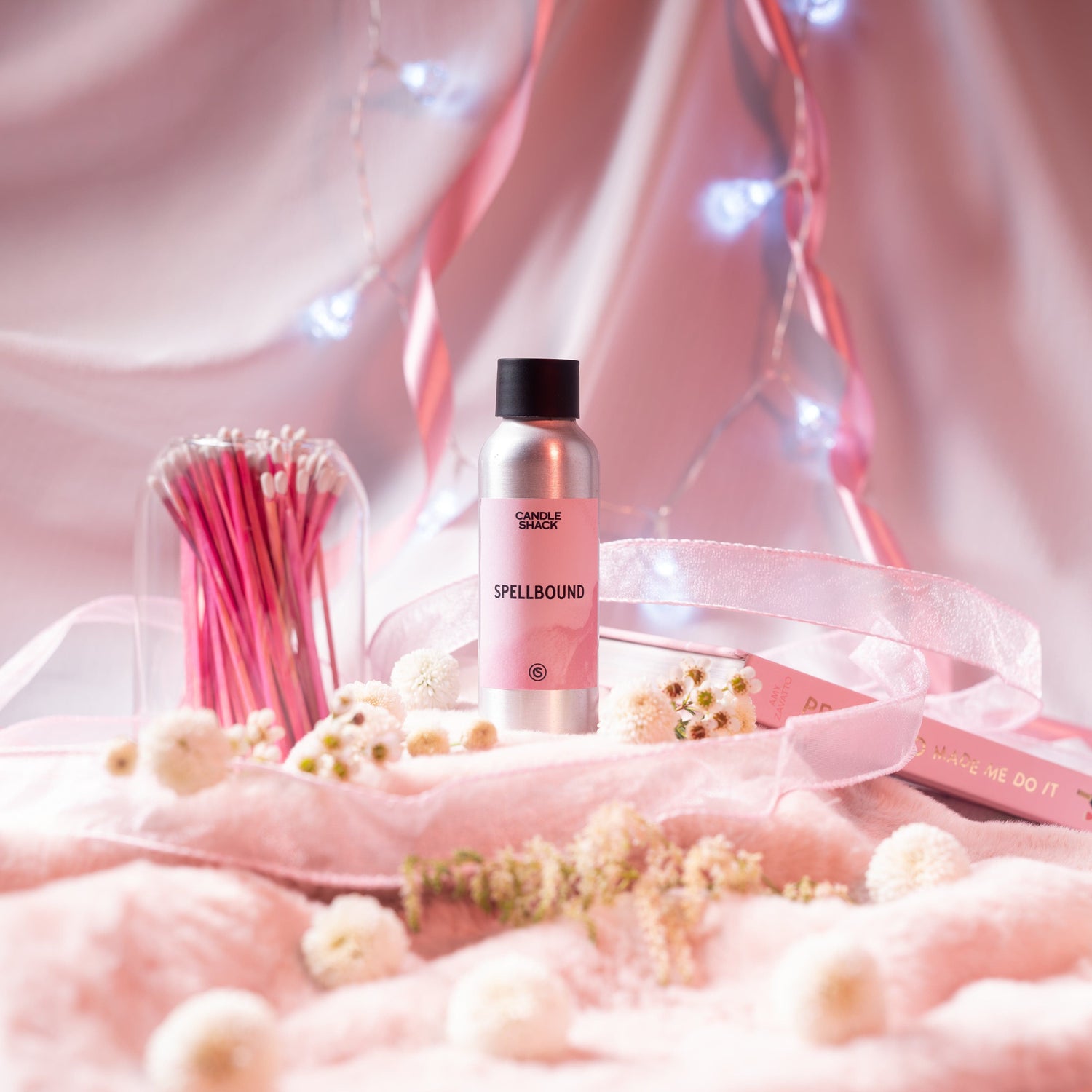 Spellbound fragrance bottle on a background of pink blankets and silks with white flowers and fairy lights.