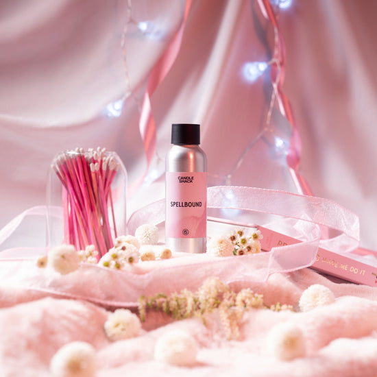 Spellbound fragrance bottle on a background of pink blankets and silks with white flowers and fairy lights.