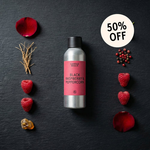 Candle with black raspberry and peppercorn fragrance oil on a dark surface with raspberries and rose petals.