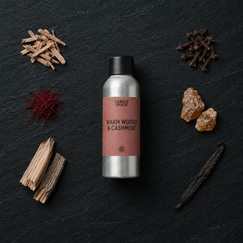 Warm Woods & Cashmere fragrance oil - Candle Shack aluminium bottle with dried botanicals on a dark slate background